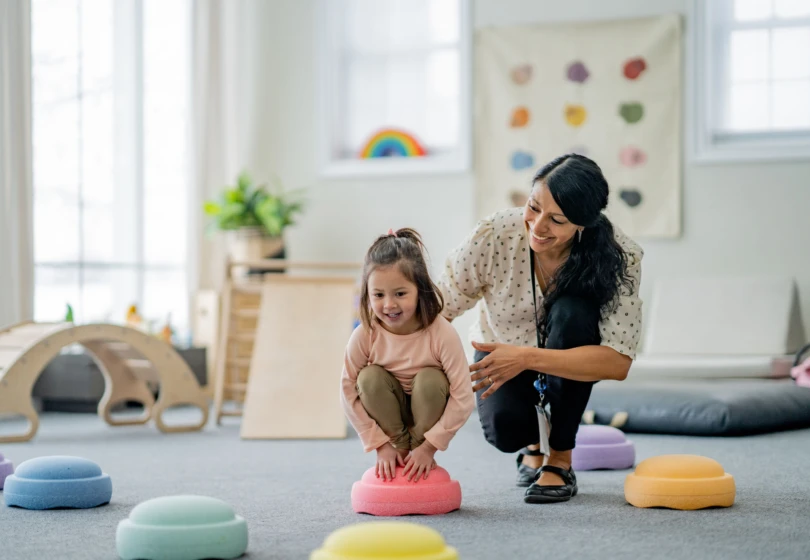 A female Physiotherapist works with a young girl on her balancing during a therapy session.  She is supporting and aiding the young girl as they work together.